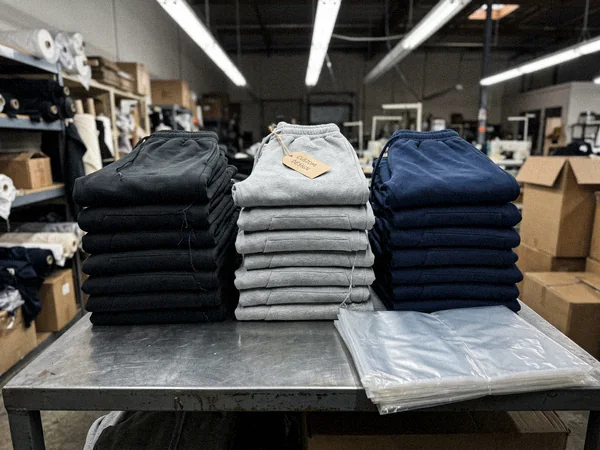 Stacks of plain blank tracksuit sets in black, grey and navy ready for decoration