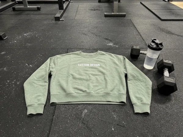 Cropped fitness sweatshirt on a gym rubber floor next to a dumbbell
