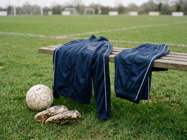 Full-zip polyester tricot track jacket and pants with side piping on a football pitch bench
