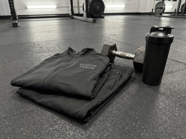 Slim stretch training tracksuit folded on a gym rubber floor next to a dumbbell